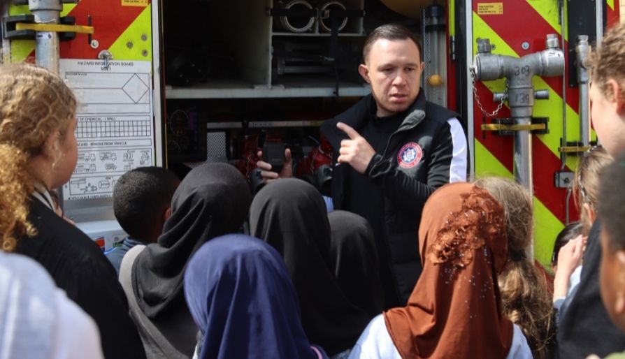 Firefighter talking to children in front of a fire engine.