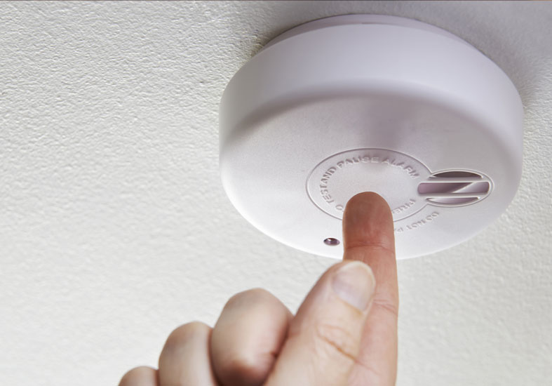 Finger pointing to fire alarm on a ceiling 