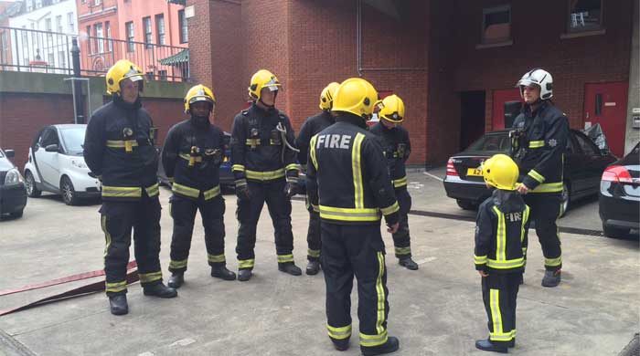 Seven firefighters in full PPE stood with a young child in a smaller version of firefighters PPE