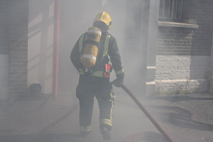 A firefighter is entering a building with smoke coming out. They are in full protective clothing with breathing apparatus 