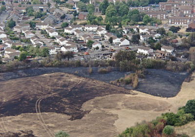 An aerial view of burnt grassland next to residential streets. The homes closest to the grassland have been destroyed.