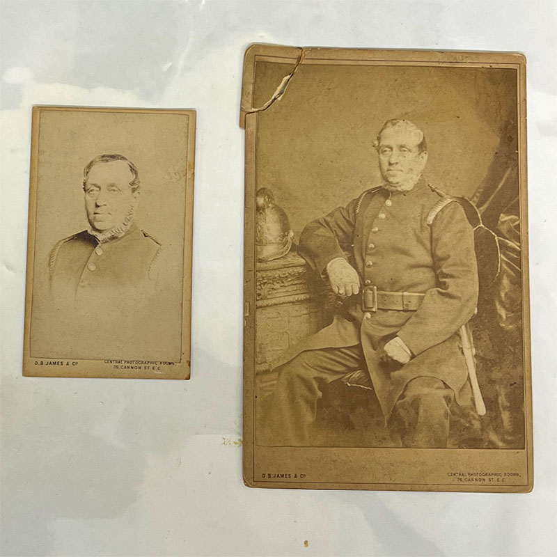 Two sepia portrait photographs of John Cliff Bridges. The first is a close up head shot. The second shows John Cliff Bridges sat on a stall in his full uniform
