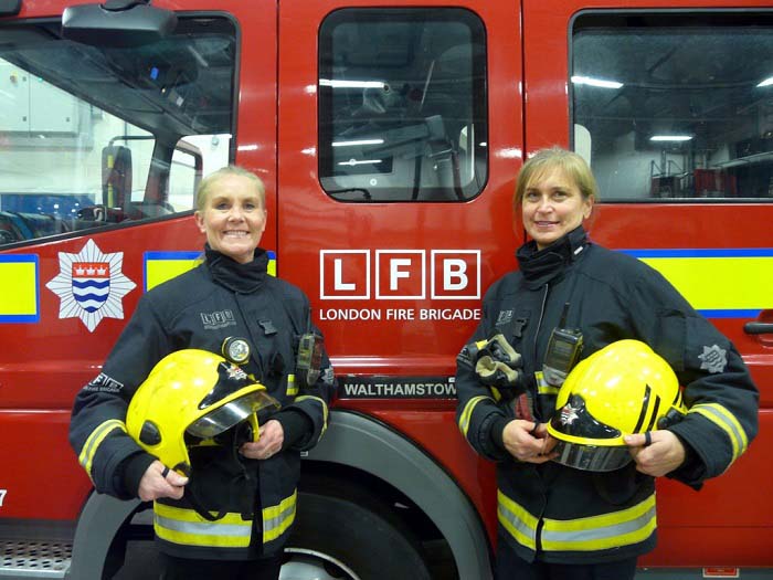 two female firefighters in PPE stood in front of a fire engine