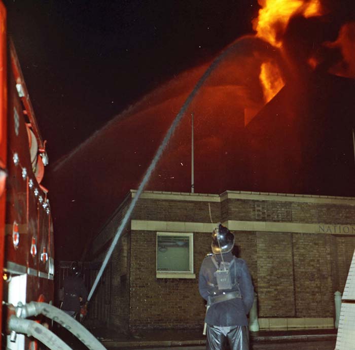 The back of a firefighter with a hose fighting the large fire at Wilson's Wharf