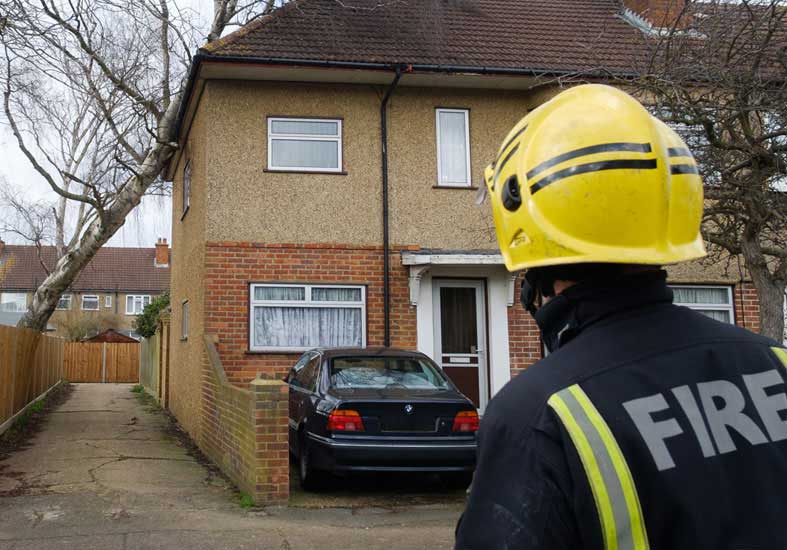 Firefighter walking up towards a house with a car parked in front of it 
