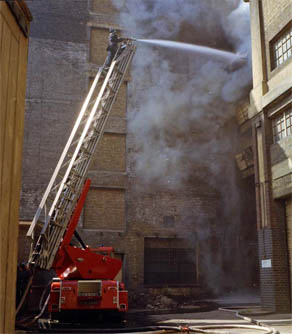 Fire at Wilson's Wharf there's a fire engine in the foreground and lots of smoke covering Town Bridge which you can see faintly in the distance