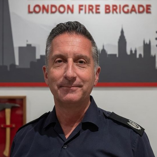 Borough Commander Paul Osborne standing in front of a wall that has a skyline of London and an axe in a presentation case.