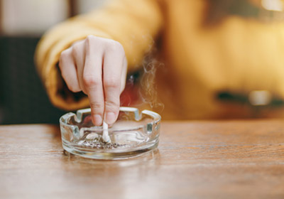 A hand stubbing out a cigarette into a heavy glass ashtray on a wooden table.
