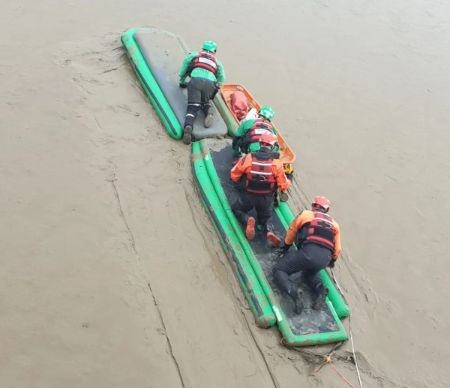 Four firefighters carrying out a rescue from mud along the Thames.