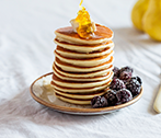 A stack of pancakes with honey and blueberry compote on the side 