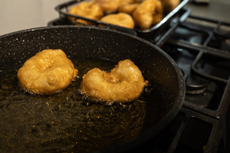 Two sufganiyots frying in a pan.