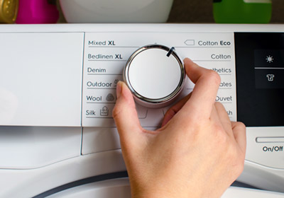 A hand turning the dial on a washing machine.