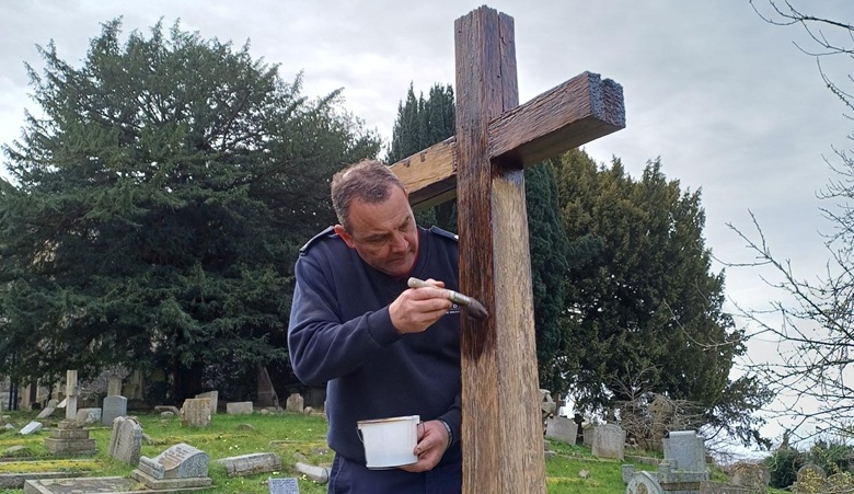 A firefighter painting a wooden cross 