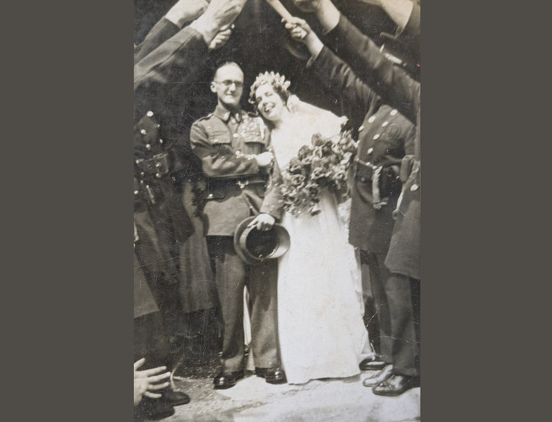Anne and George Brasnell posed for a photograph on their wedding day in 1940. They are flanked on both sides by a guard of honour of fellow Auxiliary Fire Service personnel holding their axes aloft.