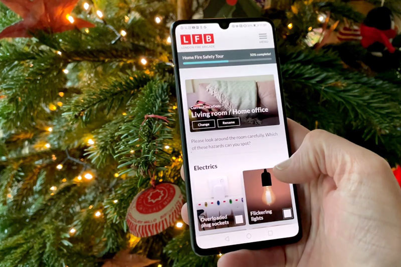 A hand scrolling through the Home Fire Safety Checker on their mobile phone, in front of a Christmas tree.