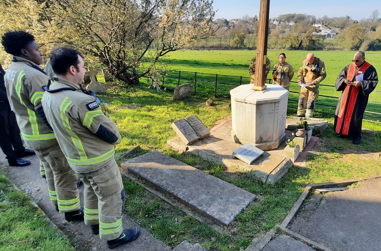 Firefighters stand either side of the cross at a graveyard 
