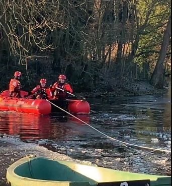 Firefighters in a boat rescuing a dog stuck in ice.