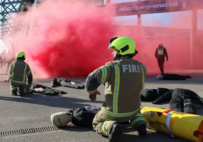 Firefighter kneeling down over a training dummy with red smoke in the background