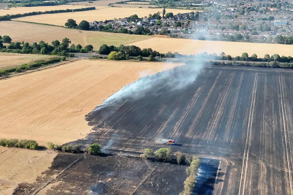 An aerial shot of a fire engine in the middle of a burnt field with light smoke coming off the grass
