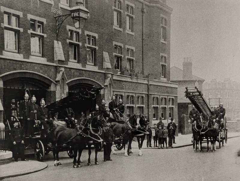 Photograph of firefighters outside Fulham Fire Station in the early 1900s, showing horse-drawn fire engines, an escape ladder appliance and station staff gathered outside the Victorian fire station.