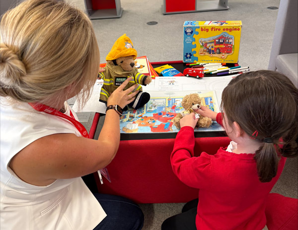 A child holding a small teddy bear with a Firesetting Intervention Scheme team member.