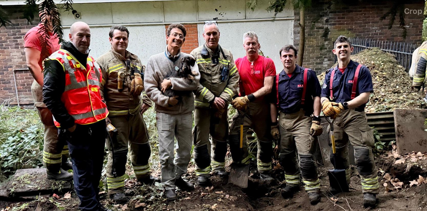 Seven firefighters and the owner holding Tosca the Dachshund