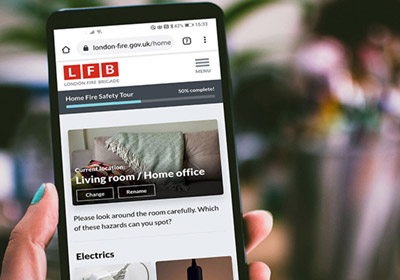 A hand holding a phone with the Home Fire Safety Checker on screen.