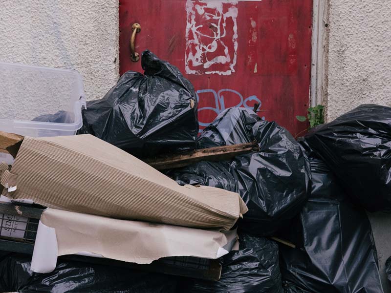 Rubbish bags, cardboard and plastic crates piled up outside an external door.