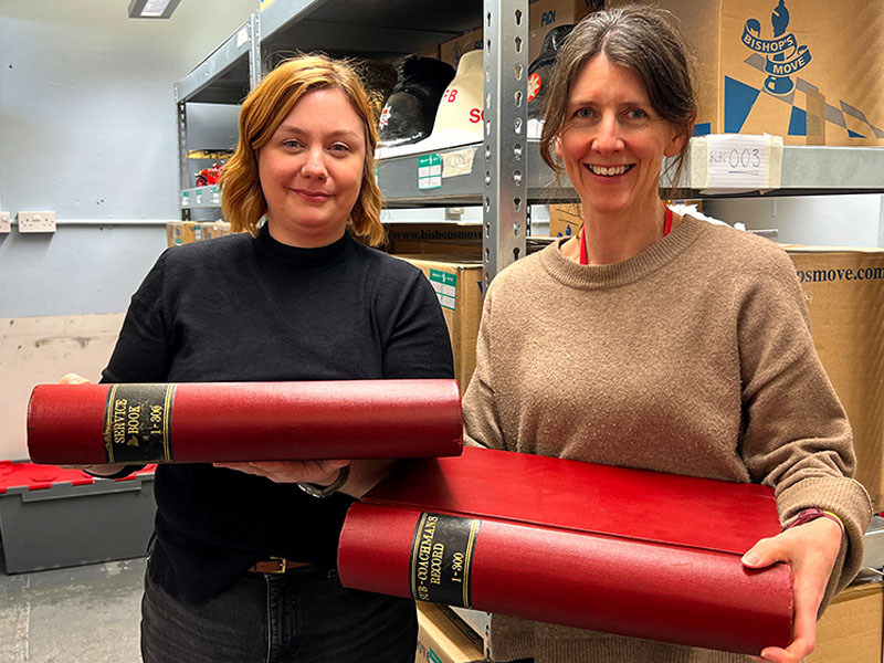 Photograph of Stephanie and Sophie from the Brigade's museum, holding two red leather ledgers containing the service records of Victorian firefighters