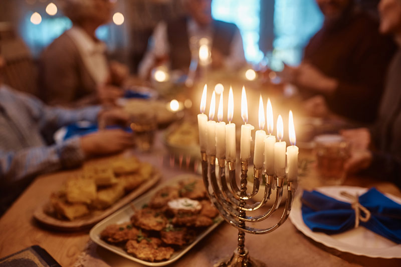 A lit menorah on a dinner table laid with many different dishes, and lots of people sitting around it.