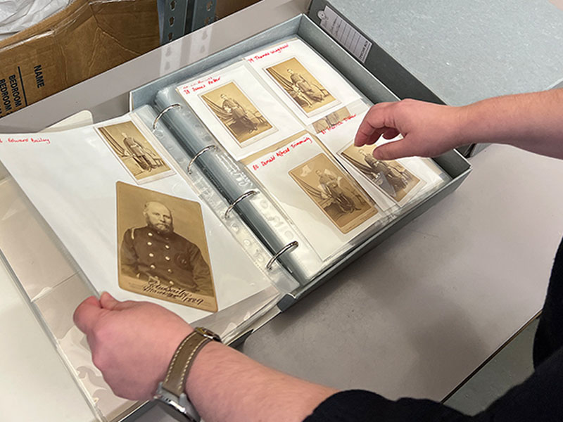 A photograph showing an open binder, containing plastic sheets. Each sheet holds a series of sepia portrait of Victorian firefighters 