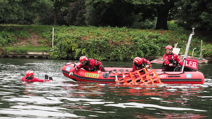 Three firefighters in an inflatable rescue boat on the water rescuing a firefighter in the water wearing a life jacket as part of a training exercise.