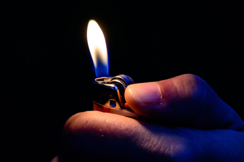 A hand holding a lit cigarette lighter.