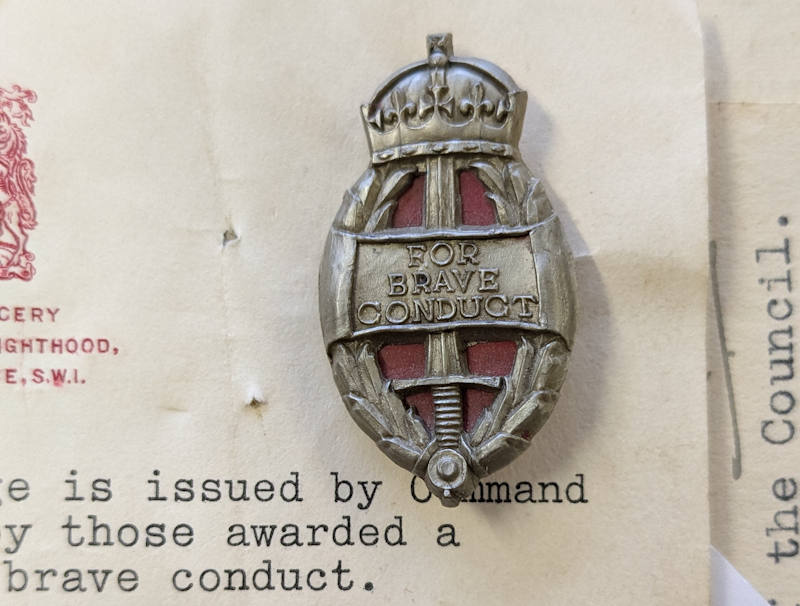 Brave Conduct Badge awarded to Auxiliary Fire Service Firewoman Anne Brasnell in 1941. The badge is attached to small piece of paper with typed official information about the badge and guidance on how it could be worn.