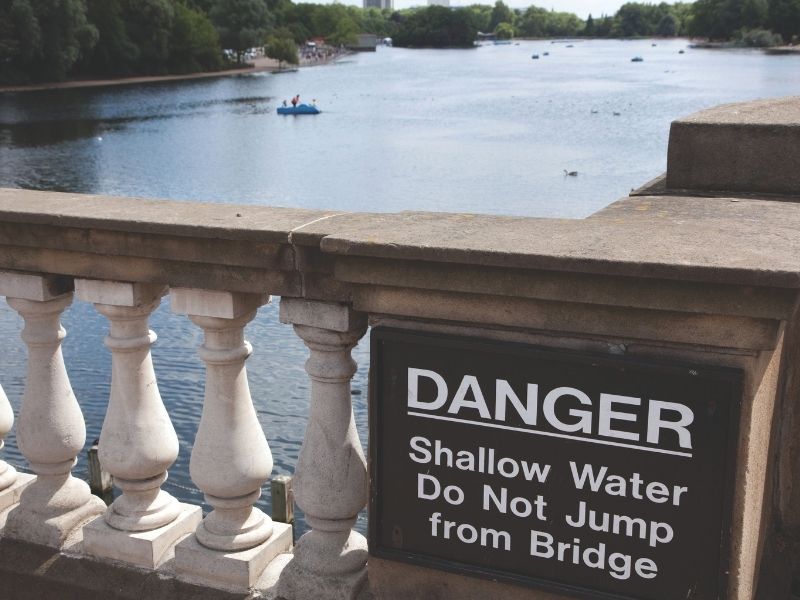 Sign on a bridge over a river that reads - danger, shallow water, do not jump from bridge.