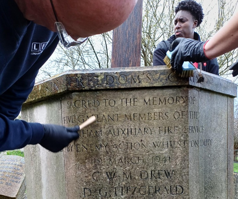 Inscriptions on a stone being cleaned by two firefighters