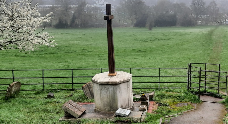 A large cross and memorial just before a large field in a graveyard