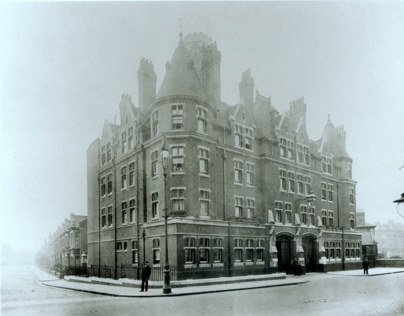 Photograph of Fulham Fire Station around 1900, showing the newly opened red-brick fire station with its distinctive corner tower and main appliance entrances on a prominent street corner site.