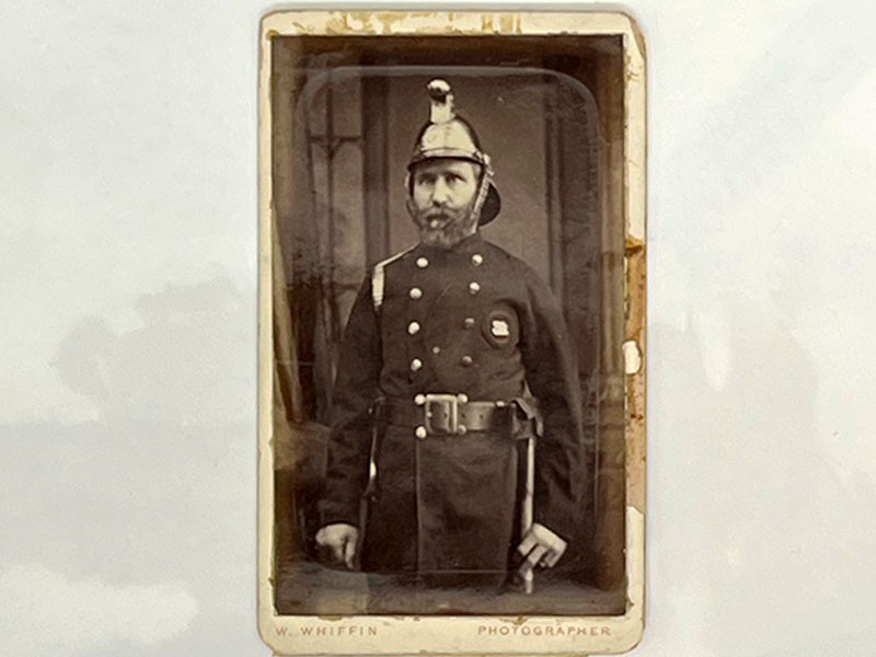Black and white photograph of John E Barker. Barker is stood to attention in his uniform