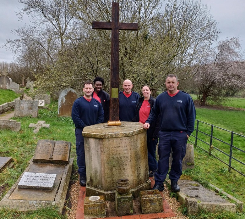 Five firefighters standing next to a memorial in a graveyard