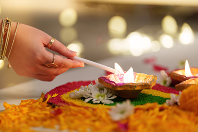 A hand lighting a diya with a taper.