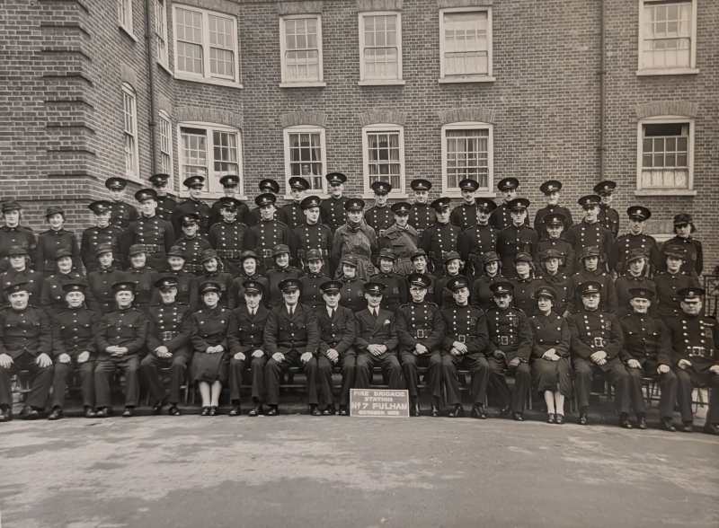 Group photograph of Auxiliary Fire Service personnel at Fulham Fire Station in 1939, showing firefighters and support staff gathered together during the early months of the Second World War.