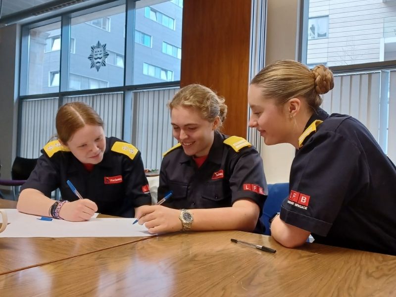 Three fire cadets sitting around a table working on a large piece of paper.